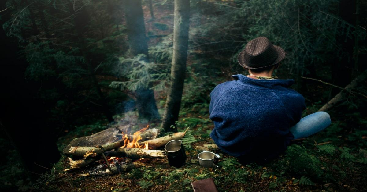 man sitting outside in a forest with a fire